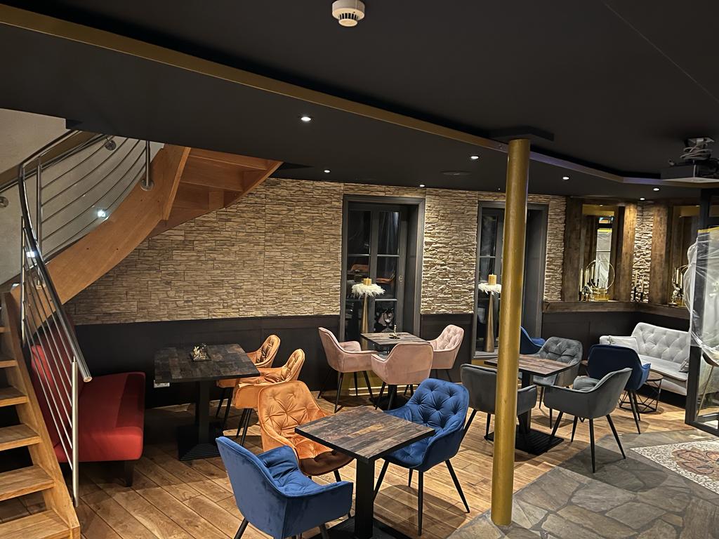 Gemütliches Café mit bunten Sesseln, Holzboden, dekorativer Steinwand und Treppe