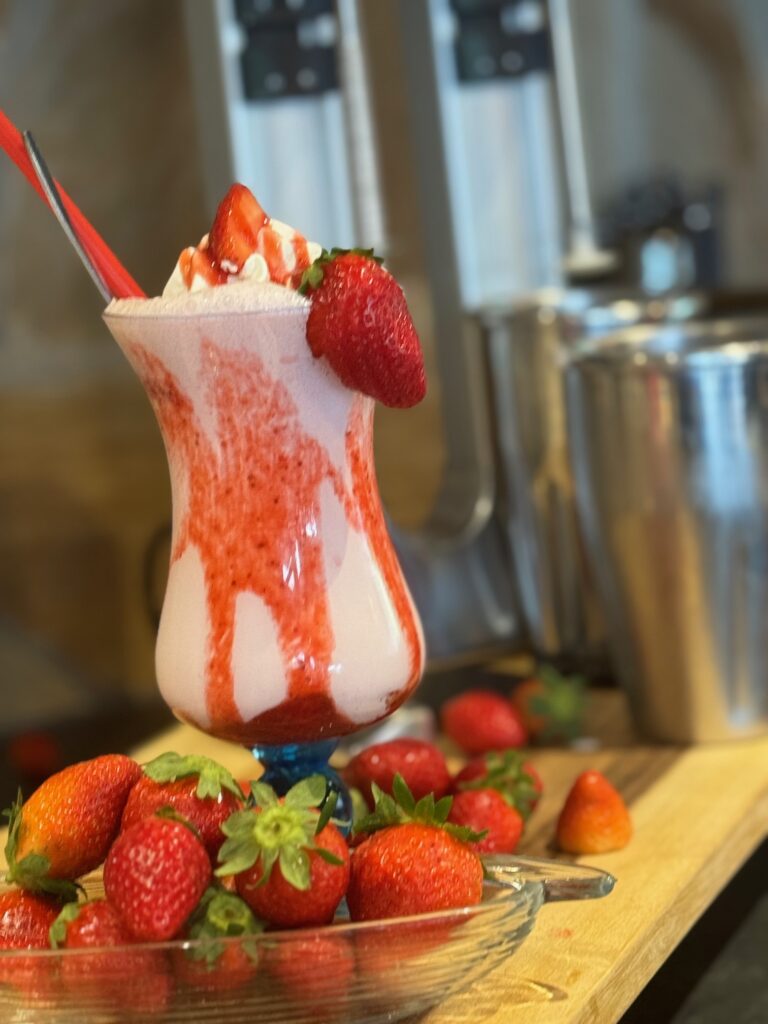 Ein cremiger Erdbeermilchshake mit Sahne und Erdbeeren in einem bauchigen Glas