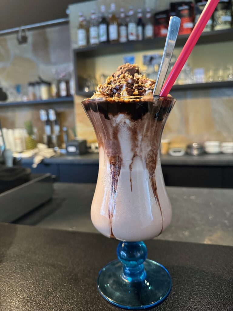 Ein Glas mit heller Schokomilch und Sahne, dekoriert mit Schokosauce und Nüssen