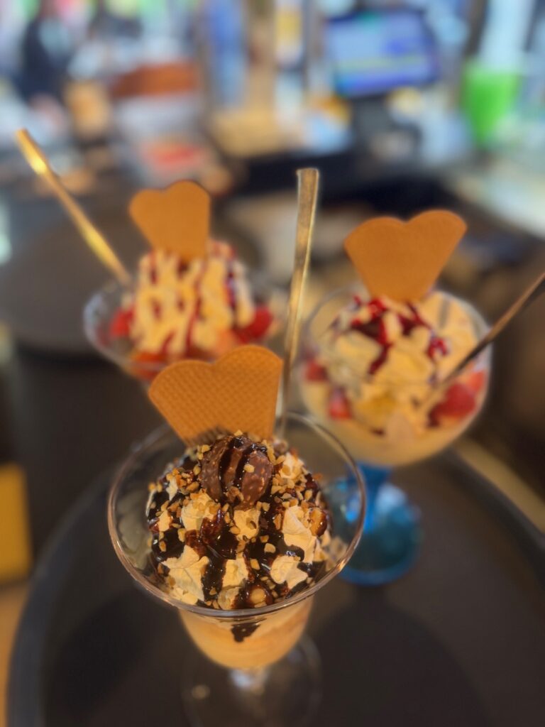 Drei bunte Eisbecher mit Sahne, Waffeln und Saucen, liebevoll angerichtet